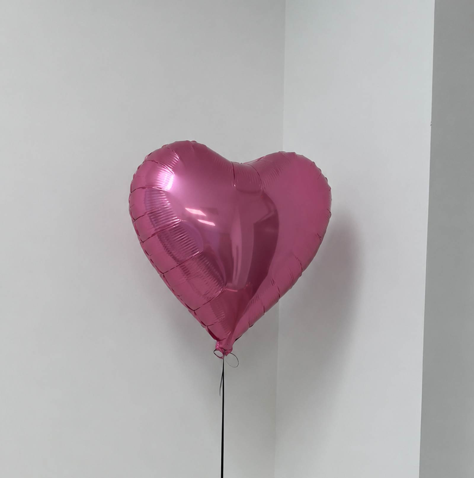 Pink heart-shaped balloon against a white wall