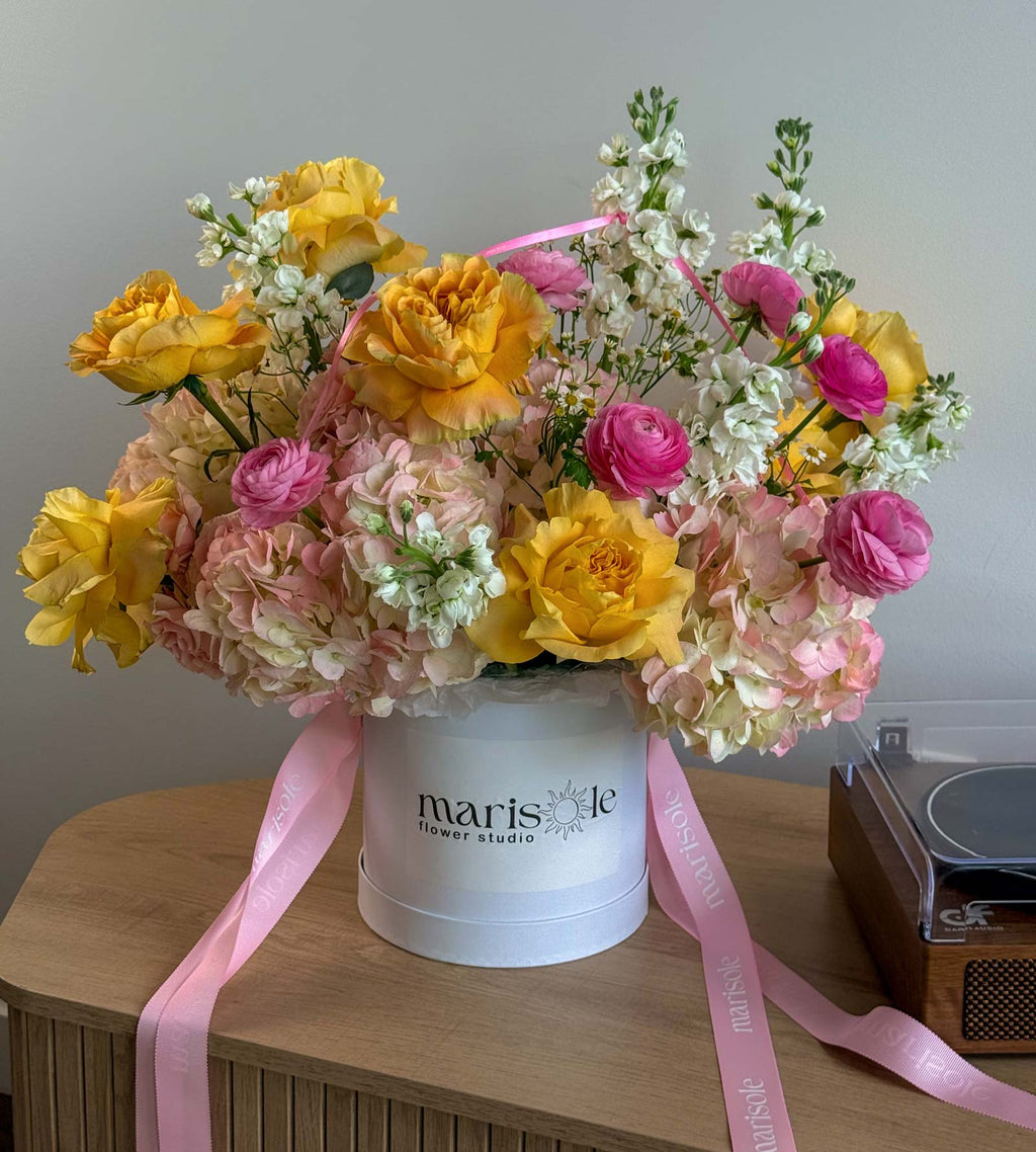 Pink Lemonade Box in a white Marisole Flower Studio box with yellow garden roses, pink ranunculus, hydrangeas, stock, and chamomile.