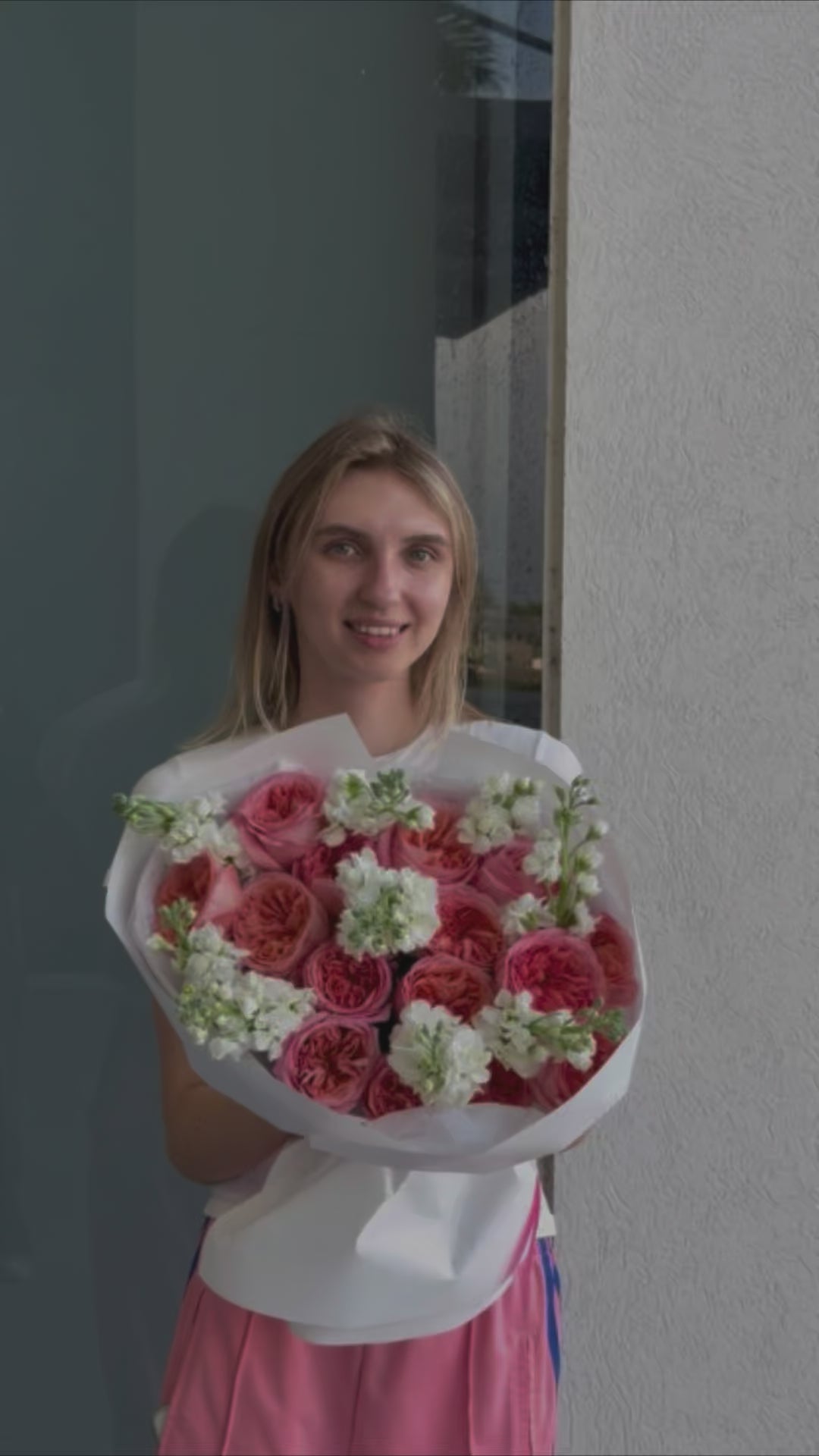 A young woman holds a large bouquet of pink roses with white filler flowers. 