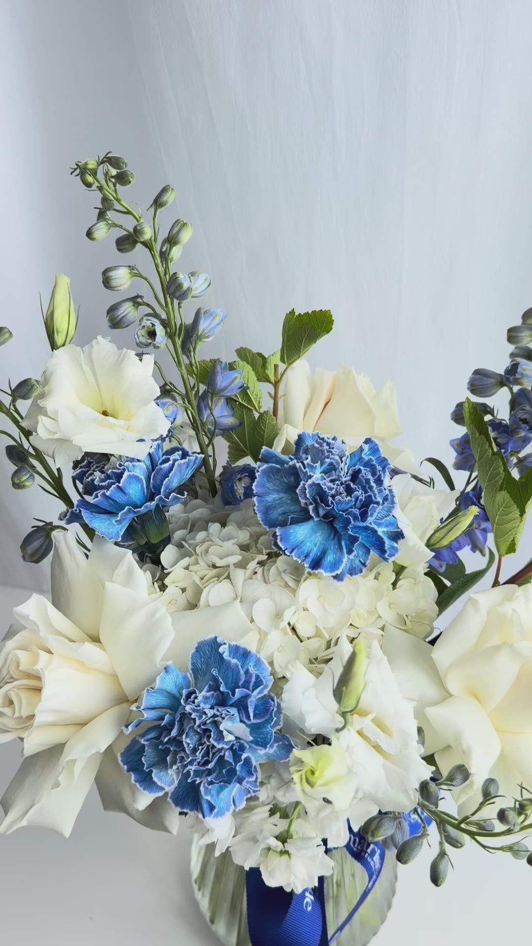 Video of the Blue Hour Vase Arrangement with blue and white flowers arranged in a glass vase.