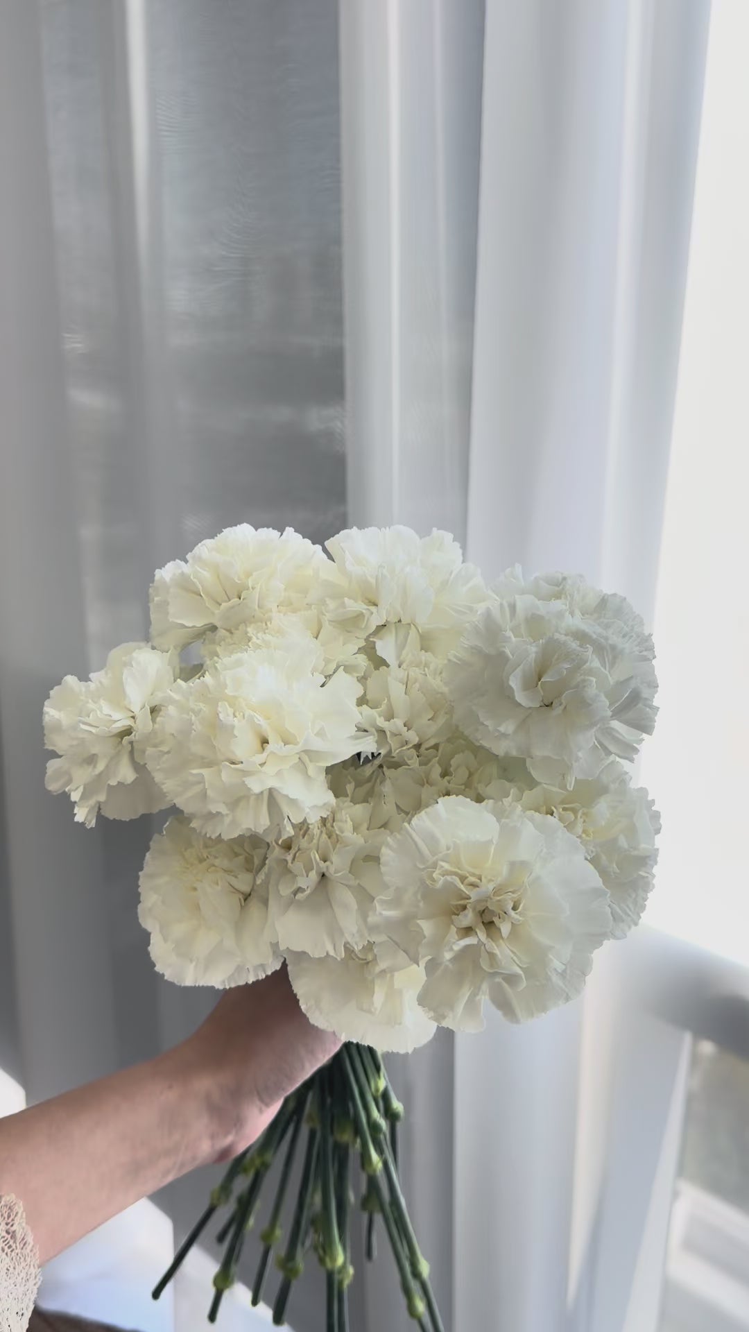 Video of a white carnation wedding bouquet with a compact rounded shape and white ribbon-wrapped stems.