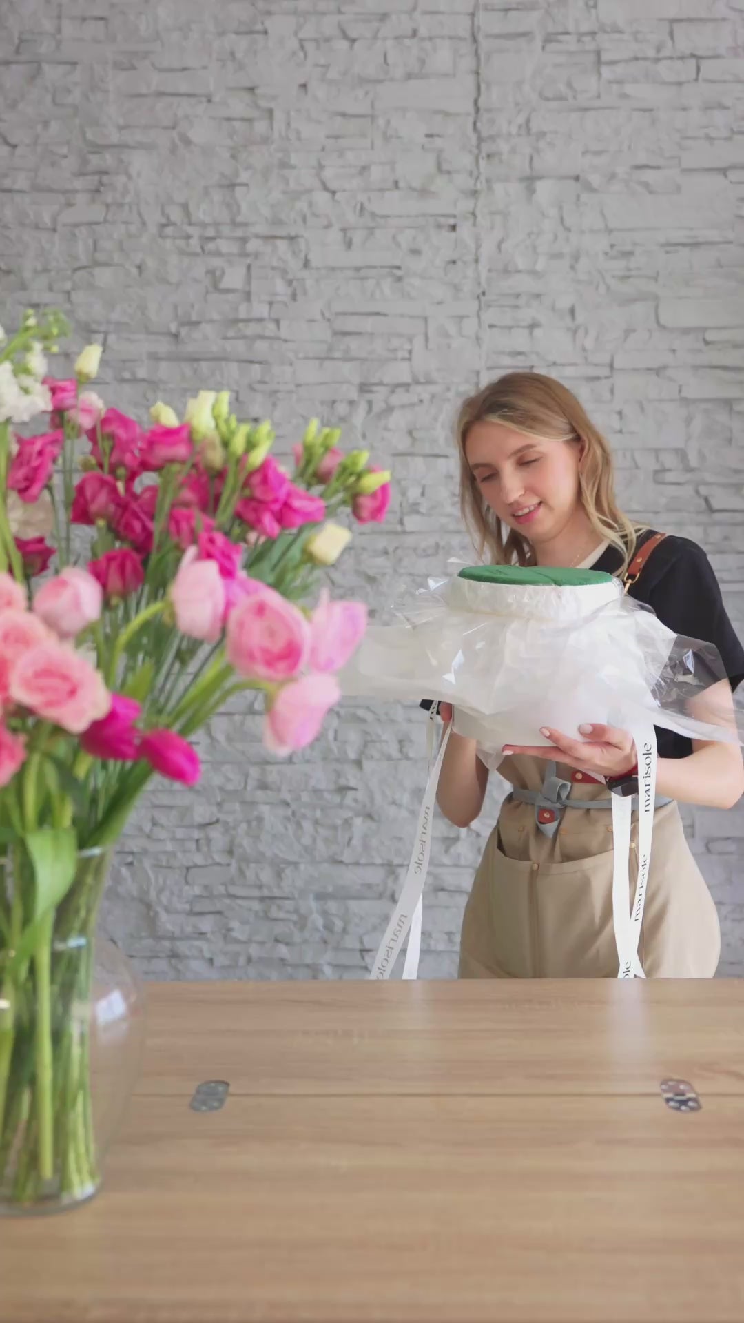 Video of a florist styling a pink flower box with pink roses, ranunculus-style blooms, and soft pastel flowers.