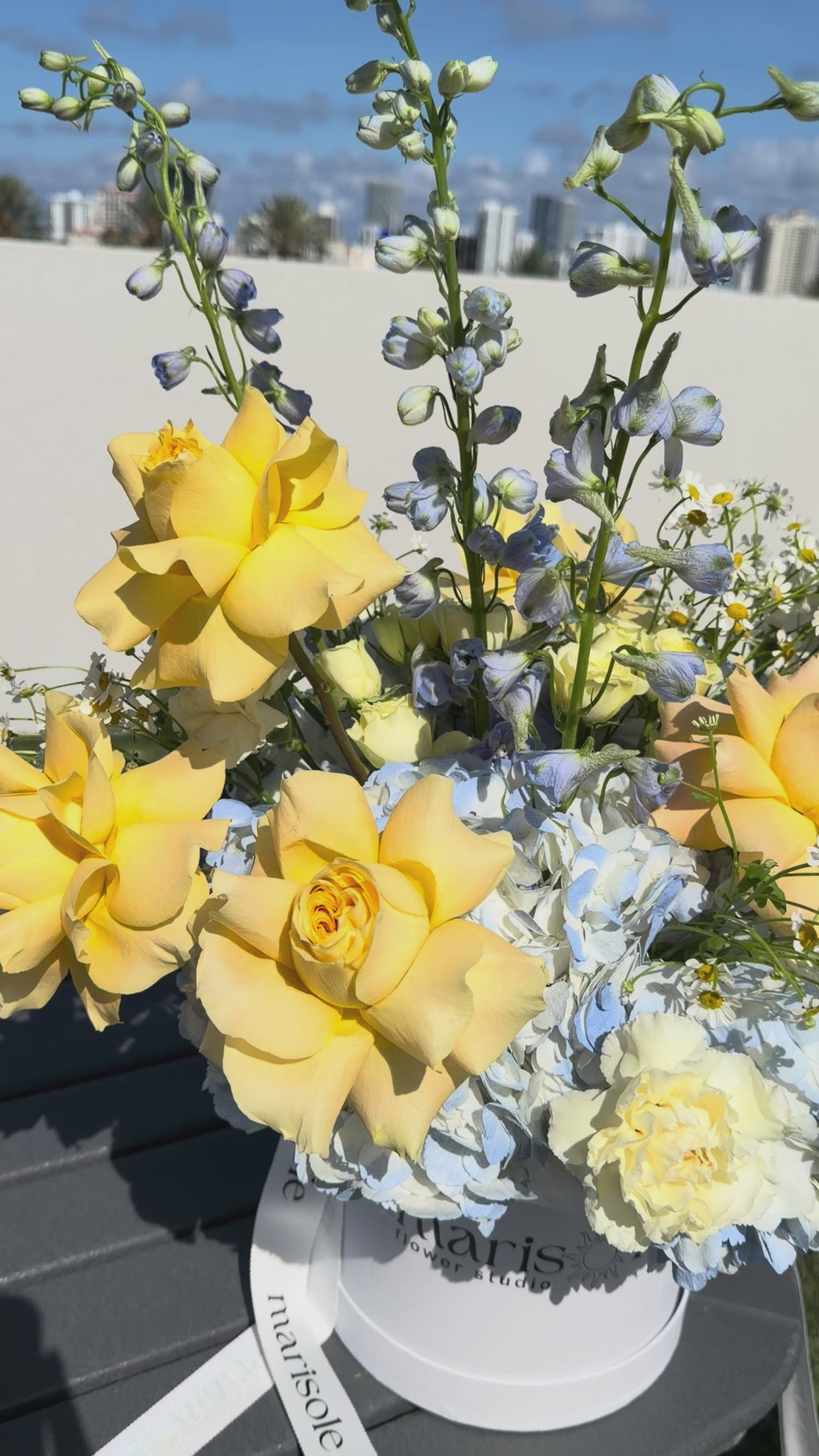 Video of the Limoncello Box by Marisole Flowers with yellow French roses, hydrangea, delphinium, chamomile, spray roses, carnations, and craspedia.