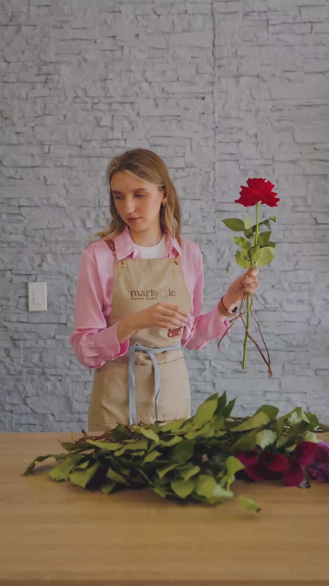 Behind-the-scenes video of a florist creating a dramatic red flower arrangement with roses and cascading floral accents.