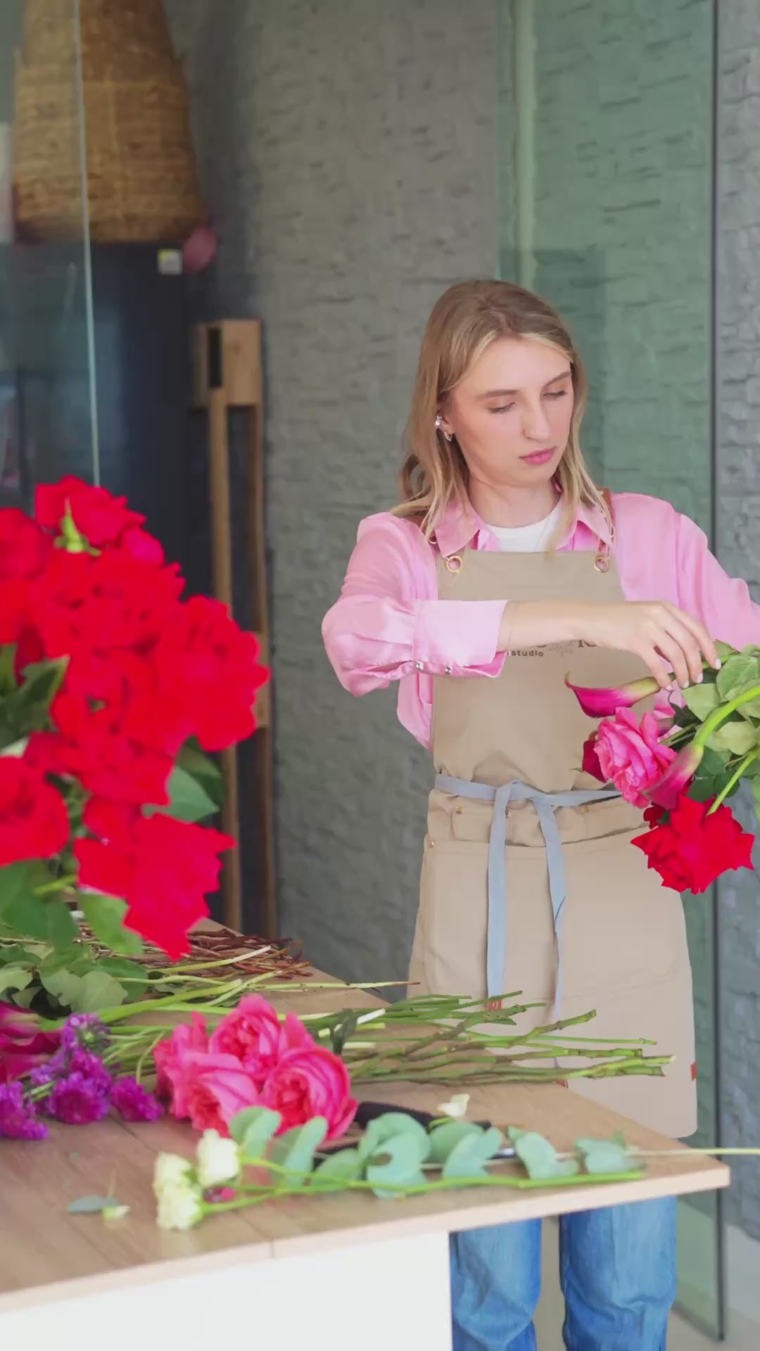 Behind-the-scenes video of a florist preparing a red rose arrangement with pink wrapping and decorative floral details.