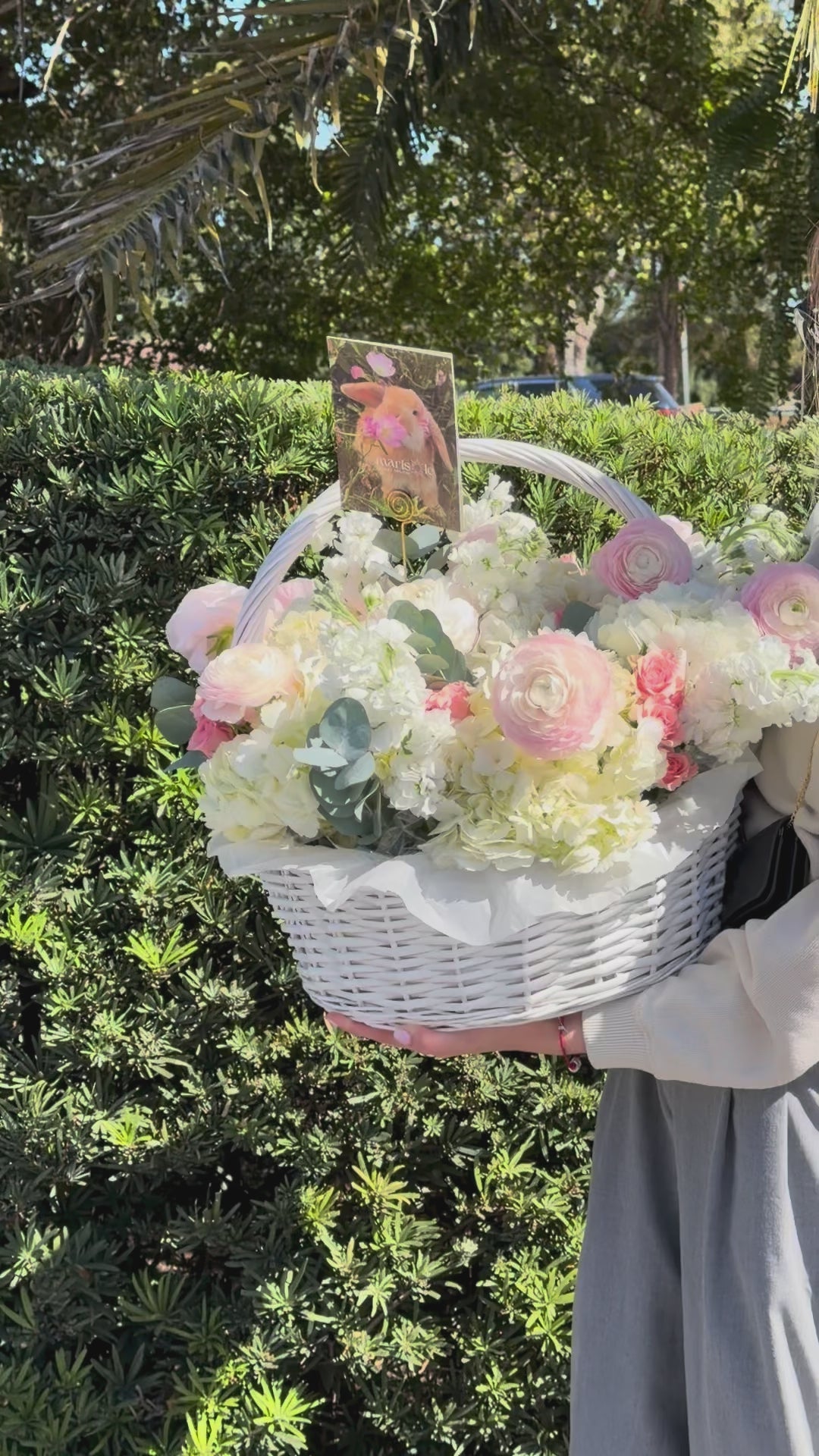 Video of a pastel flower basket with soft pink, white, and yellow blooms, styled with a greeting card for a sweet floral gift.