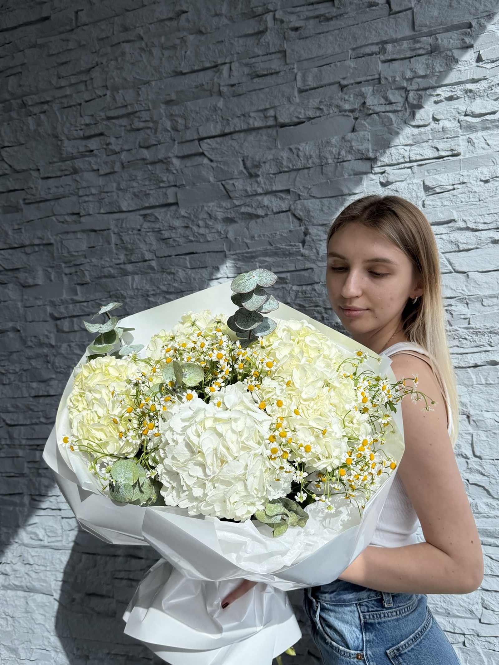 Woman holding the Pure Meadow bouquet with white hydrangeas, chamomile, and eucalyptus wrapped in white paper.