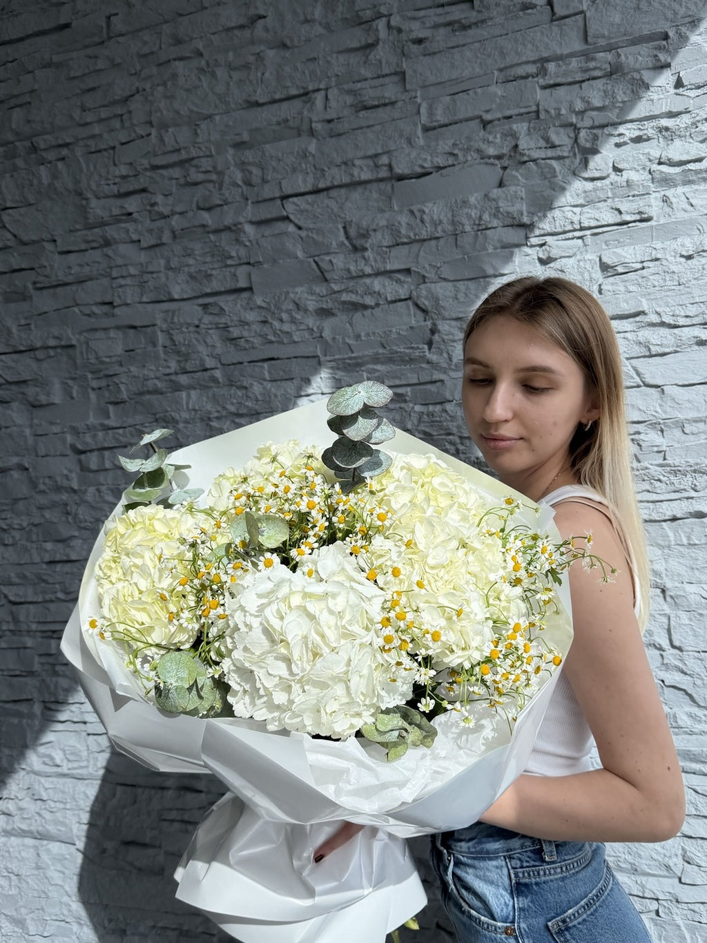 Woman holding a large bouquet of white flowers against a stone wall.