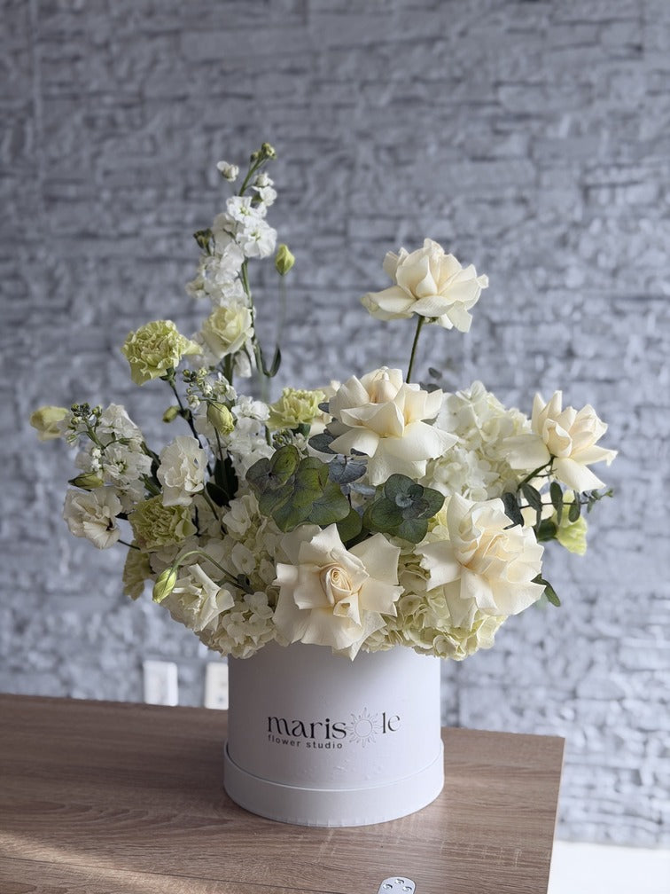 Floral arrangement in a white container on a wooden surface with a gray textured wall background