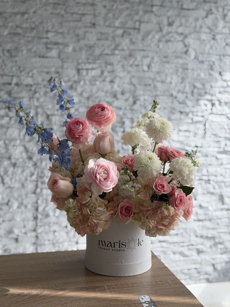 Bouquet of pink and white flowers in a white container with 'maris' on it, against a textured wall.