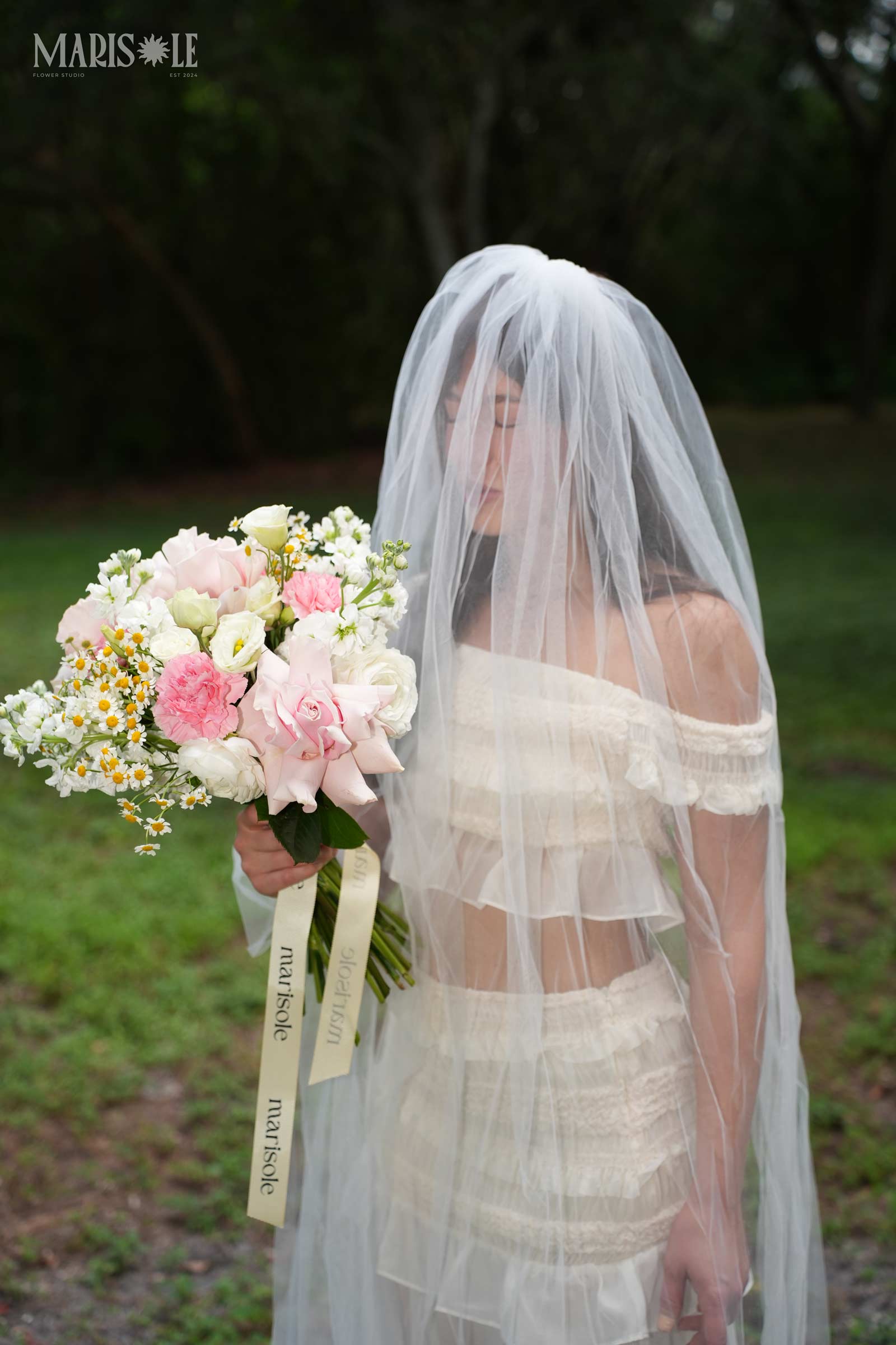 Bride holding a pastel bouquet under a soft veil outdoors