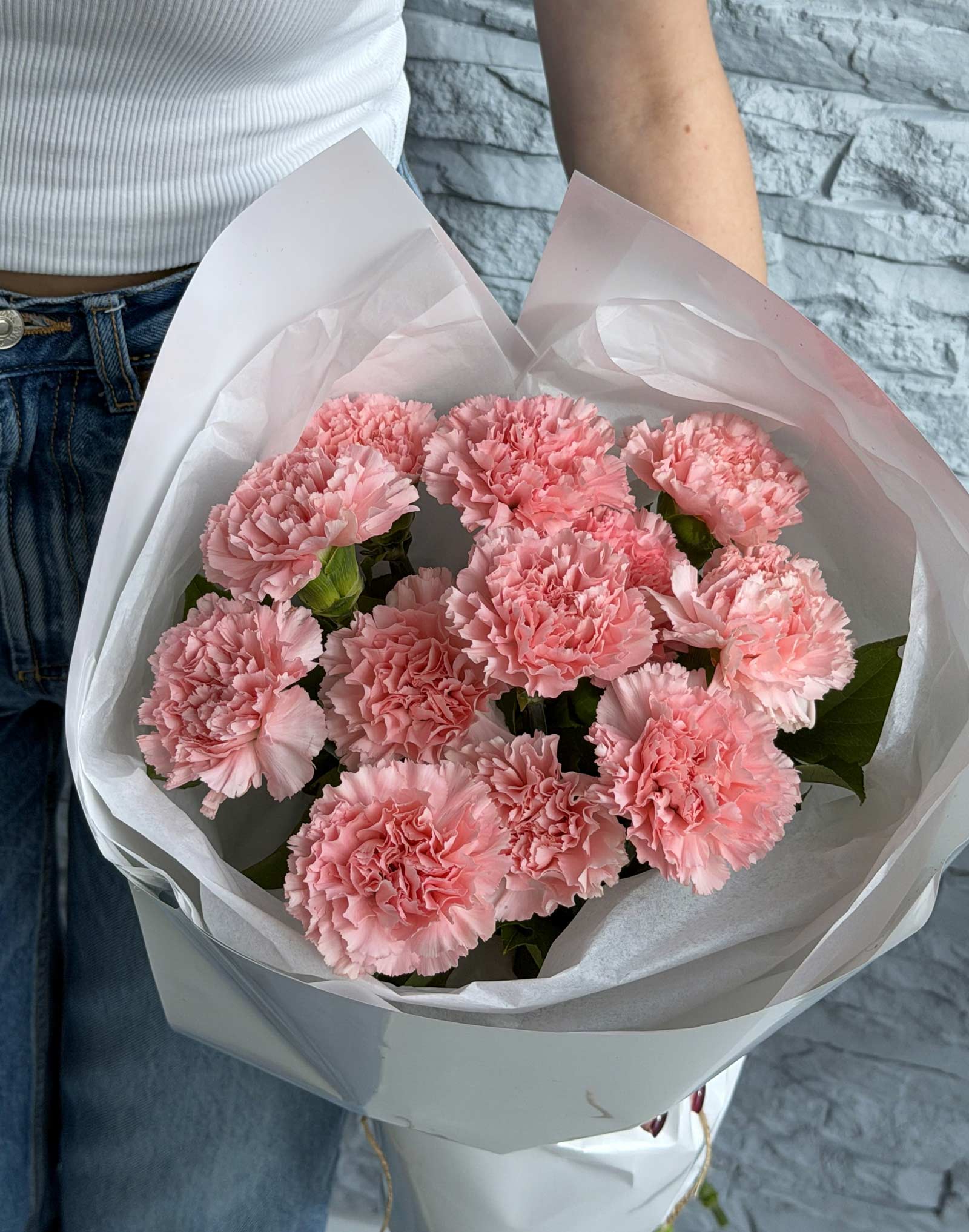 Bouquet of pink carnations wrapped in white paper held by a person.