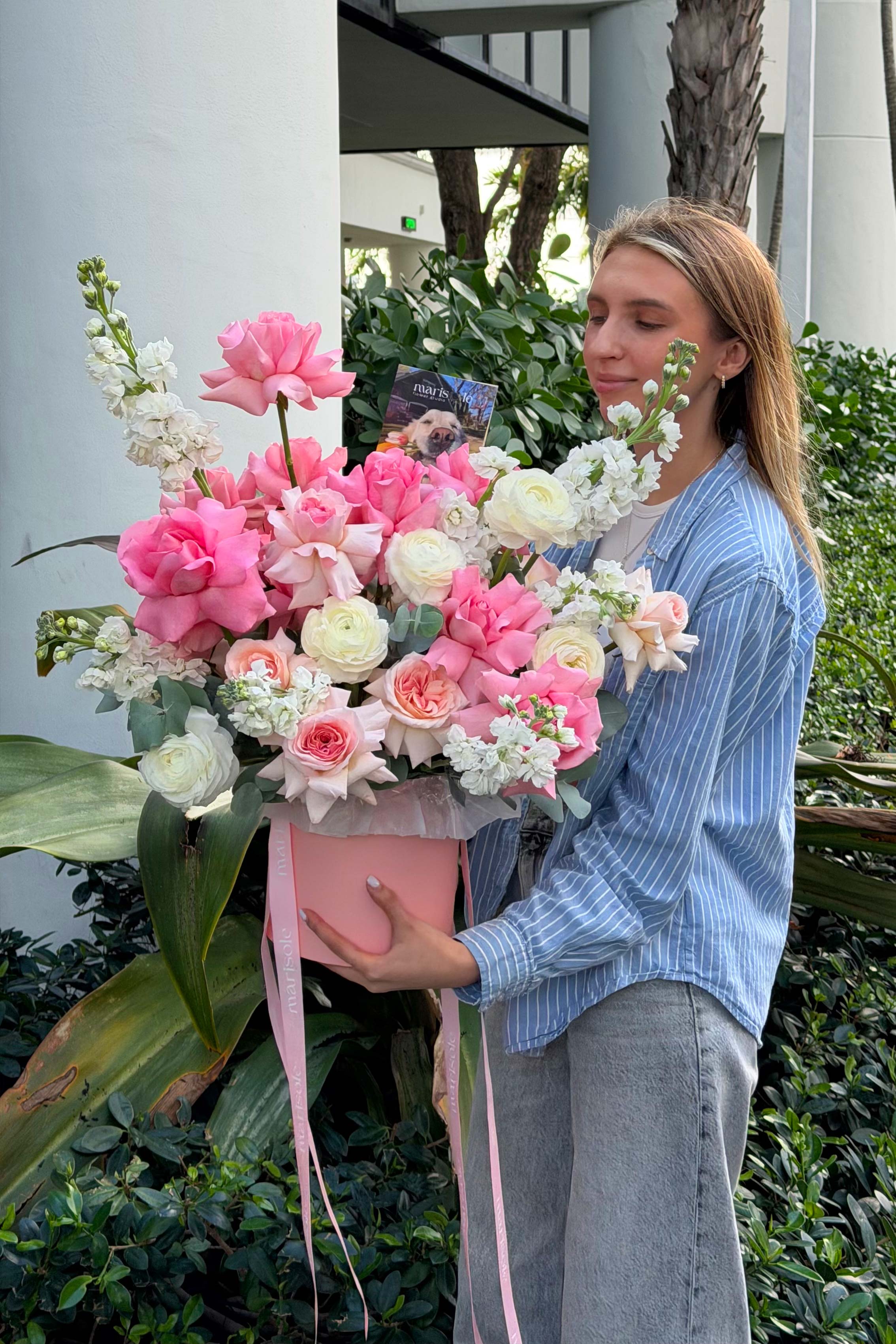 Woman holding a large bouquet of pink and white flowers outdoors.
