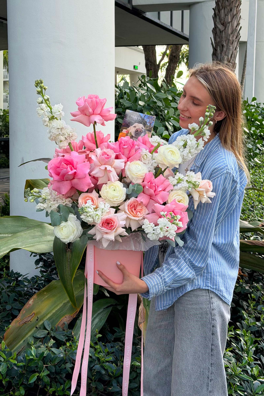 Woman holding a large bouquet of pink and white flowers outdoors.