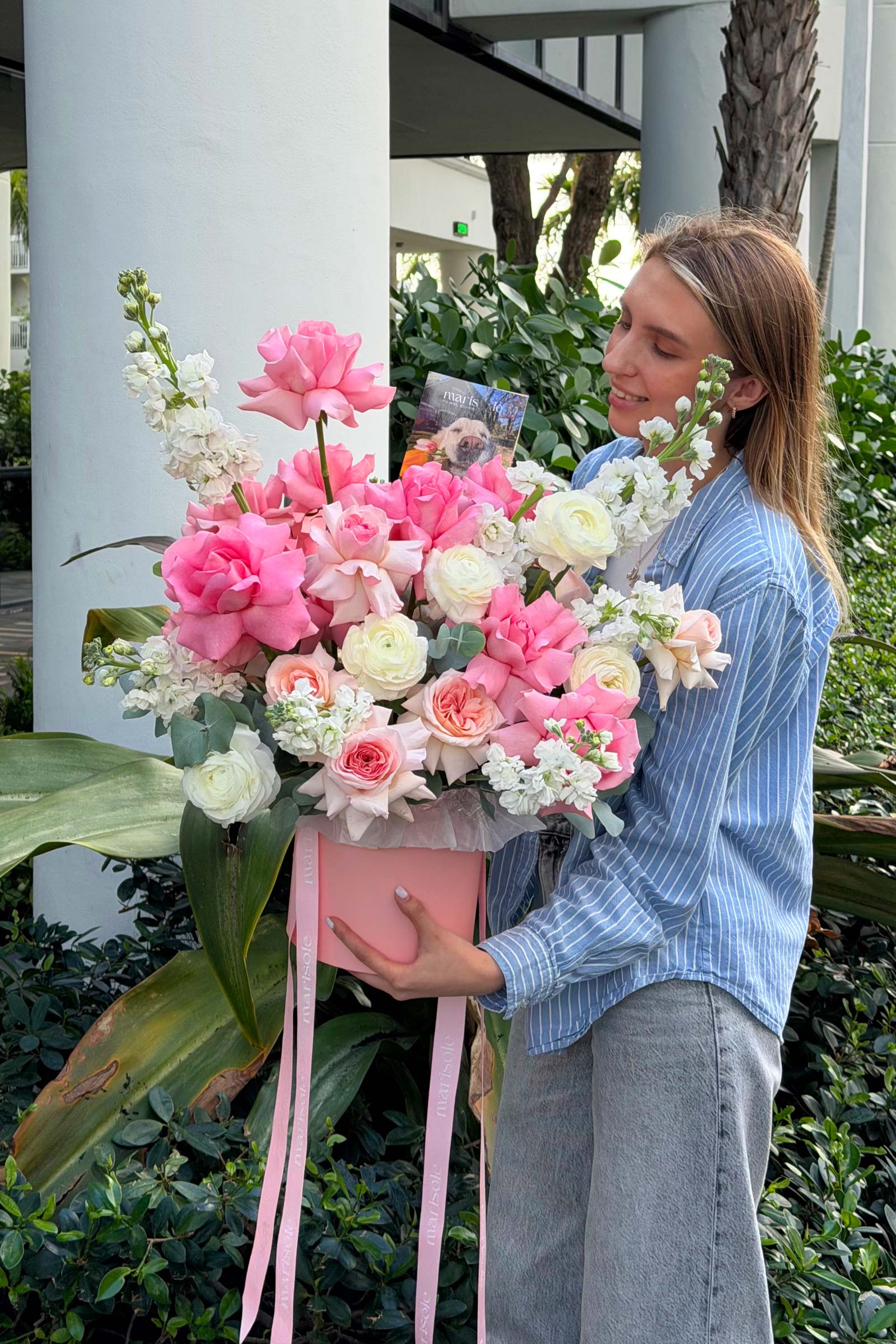 Woman holding a large bouquet of pink and white flowers outdoors.