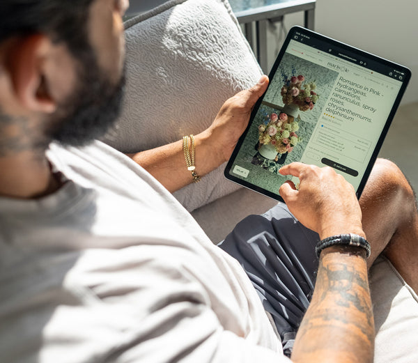 Person using a tablet on a couch with a floral arrangement displayed on the screen