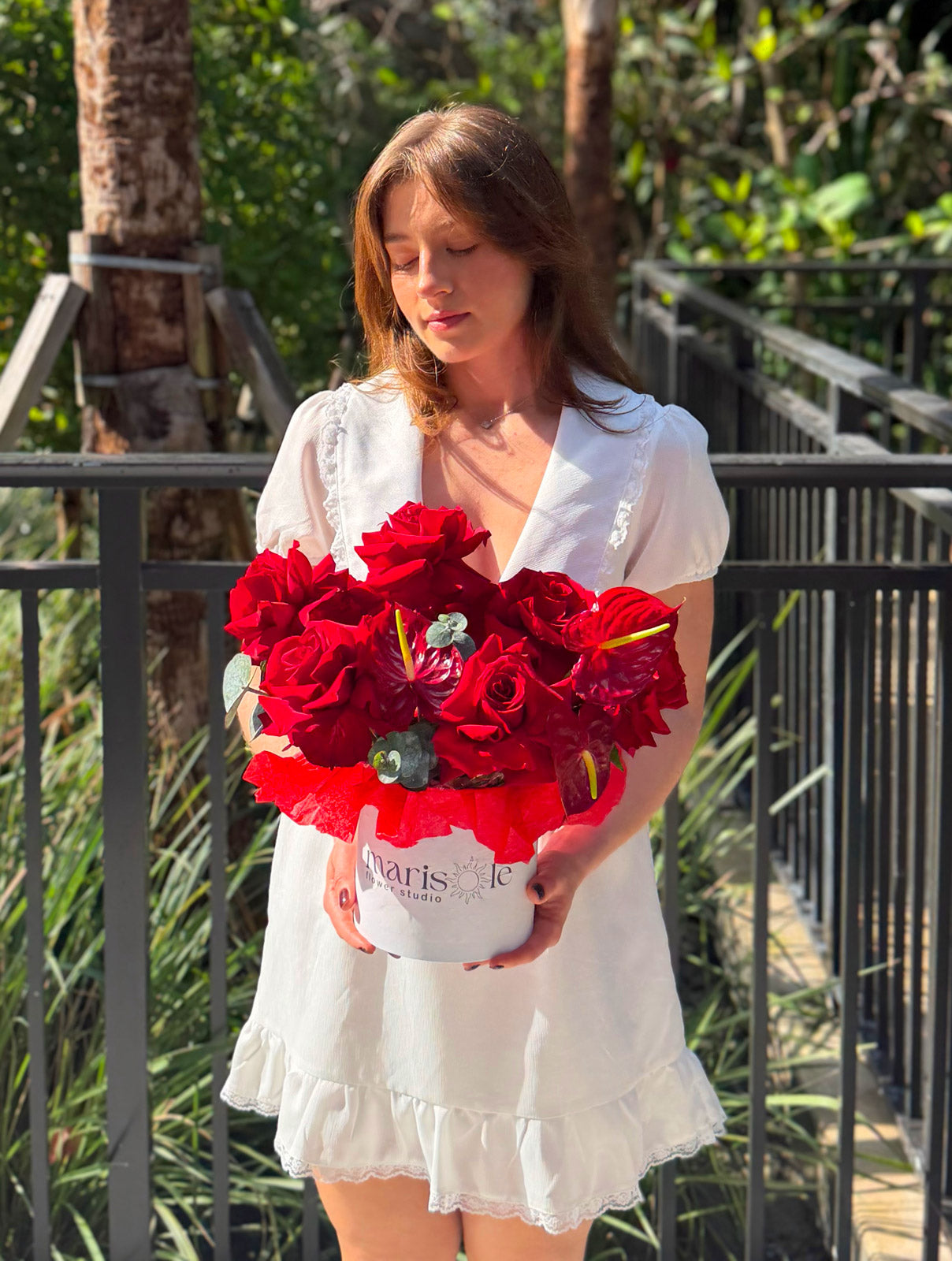 Woman holding a bouquet of red flowers outdoors with greenery in the background