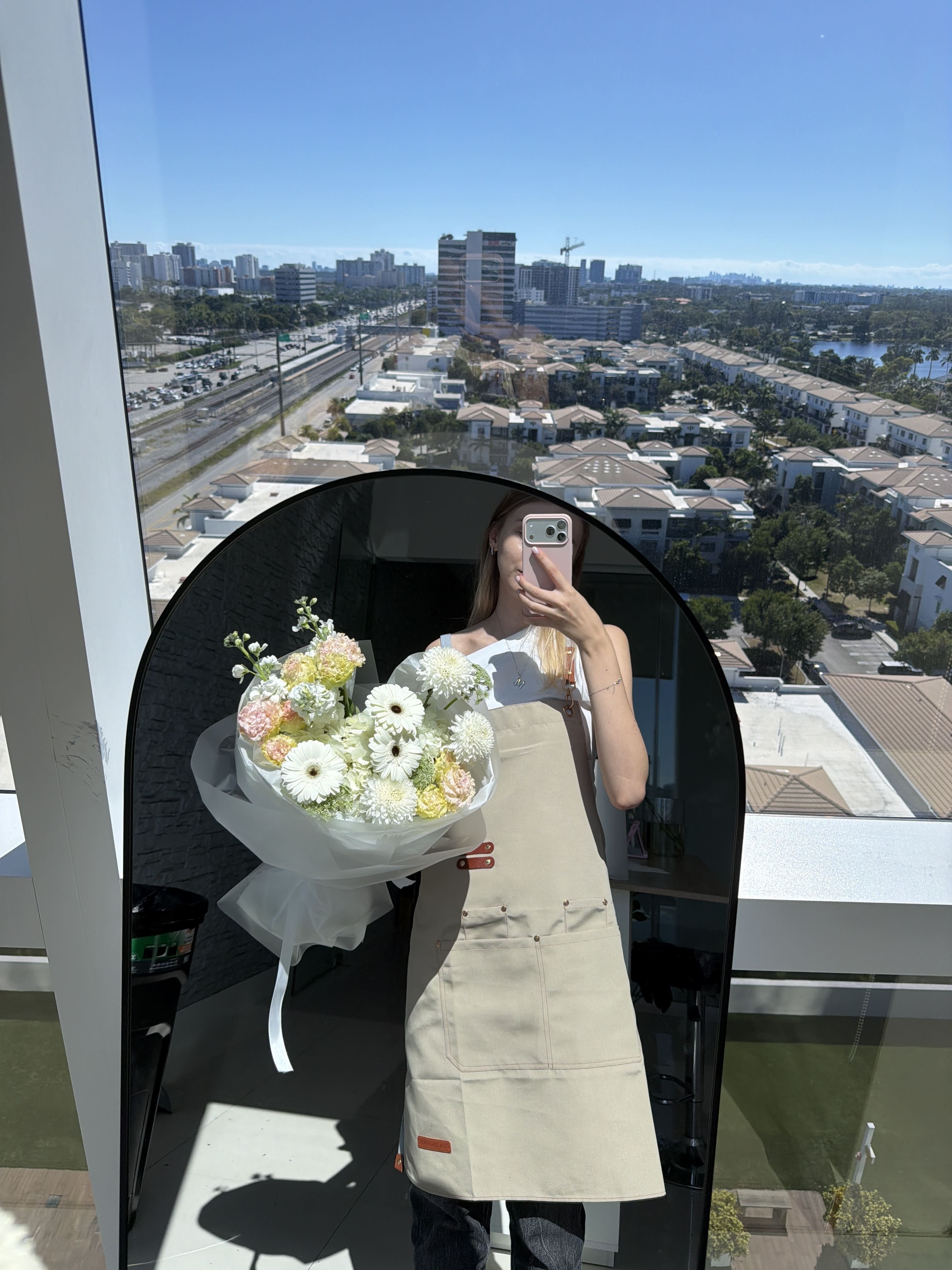 Person holding a bouquet of flowers in front of a large window with a cityscape view.
