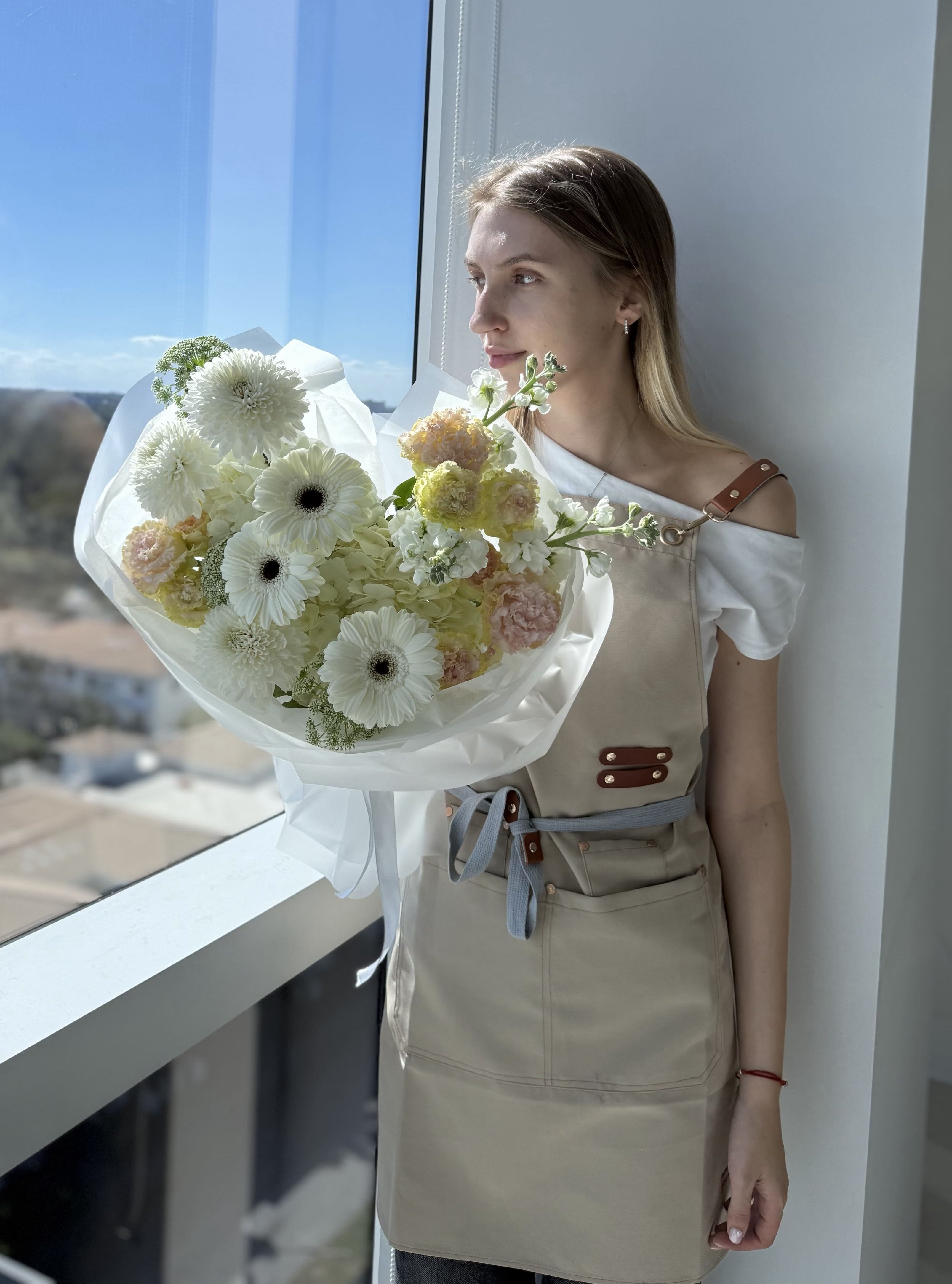 Woman holding a bouquet of flowers by a window with a scenic view.