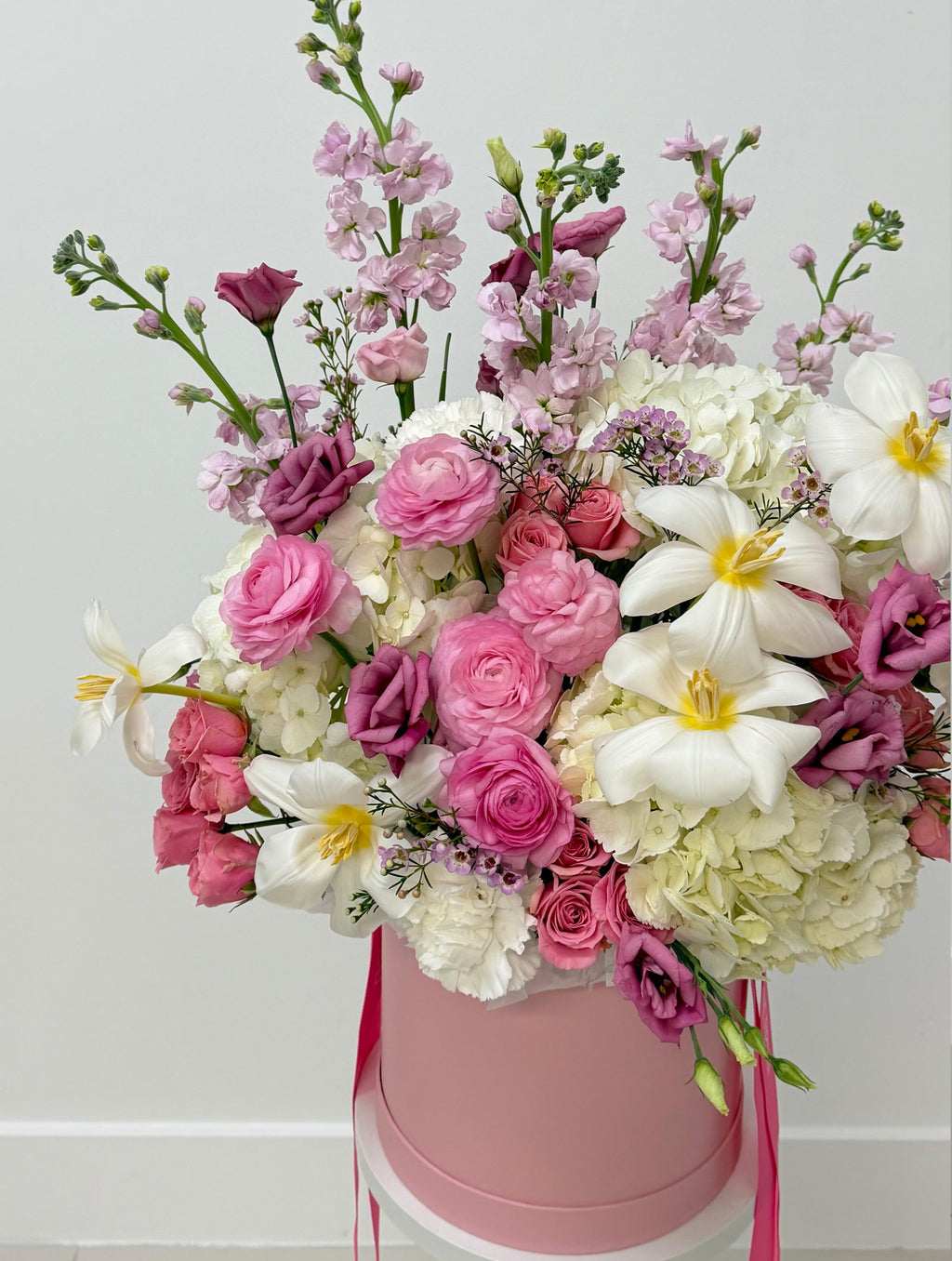 Bouquet of pink, white, and purple flowers in a pink box on a light gray background