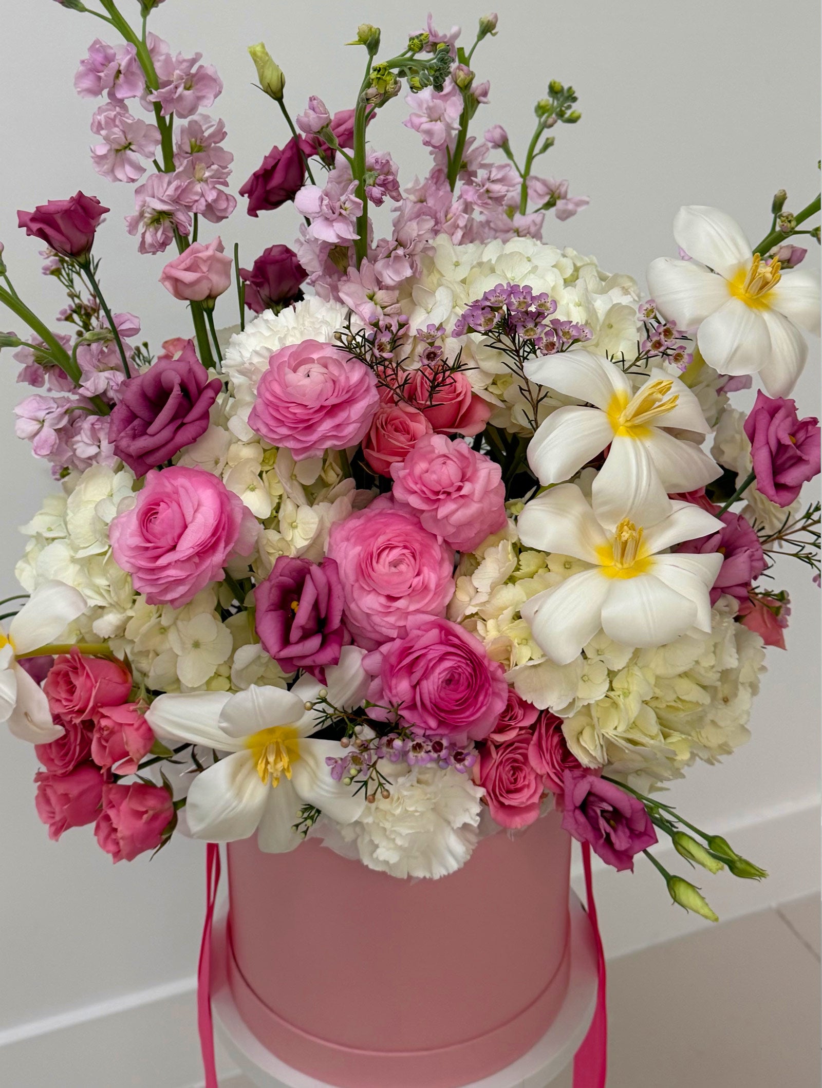 Bouquet of pink, white, and purple flowers in a pink box on a light gray background