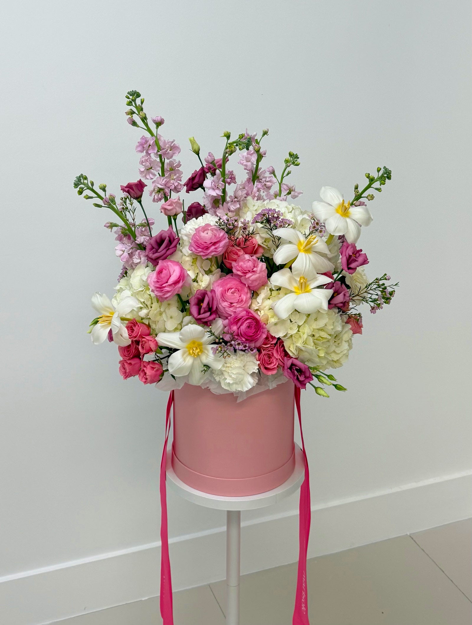 Pink flower box with a bouquet of flowers on a white stand against a light gray background