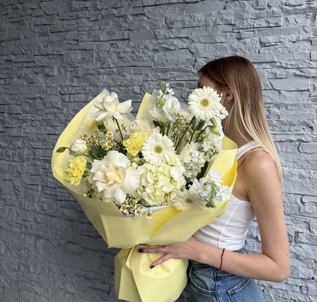 Woman holding a bouquet of white and yellow flowers against a gray stone wall.