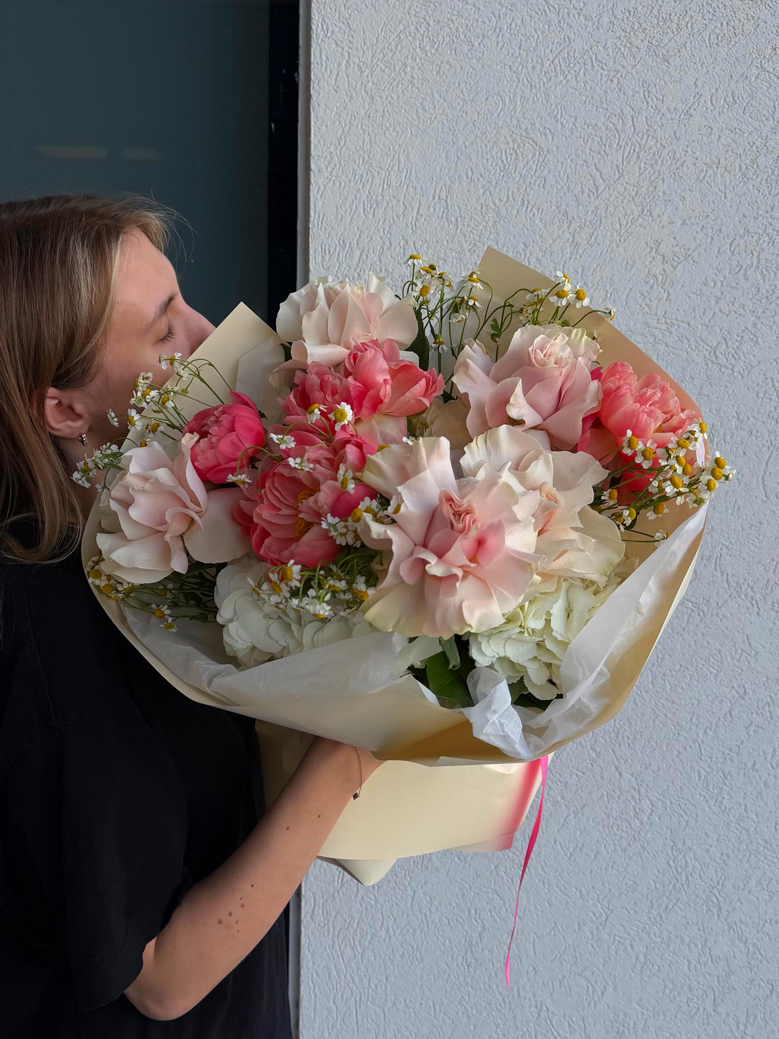 Person holding a bouquet of pink and white flowers against a plain wall.