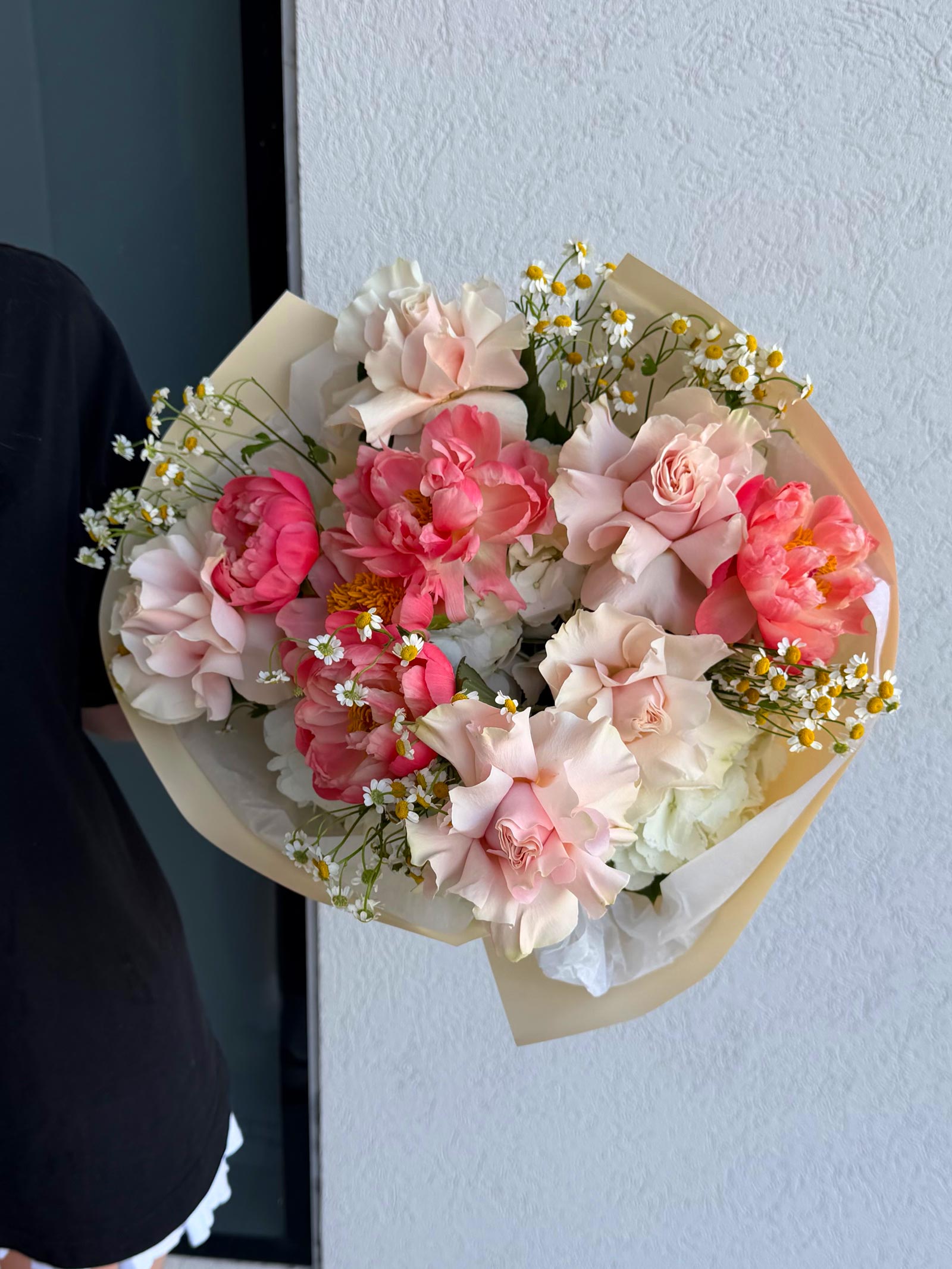 Bouquet of pink and white flowers held by a person against a light blue wall.