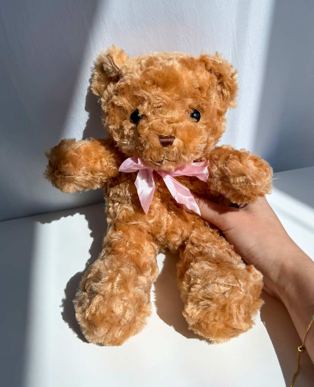 A fluffy light brown teddy bear with a pink satin bow around its neck
