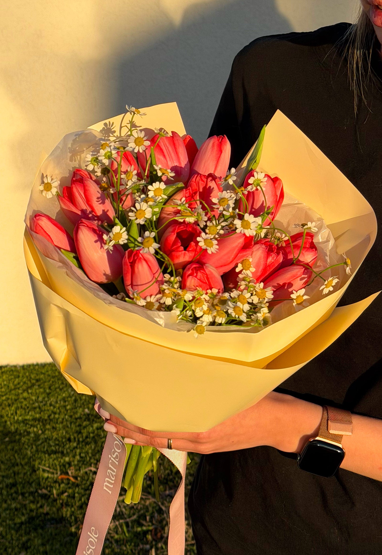 Bouquet of red tulips held by a person with a yellow wrap against a neutral background