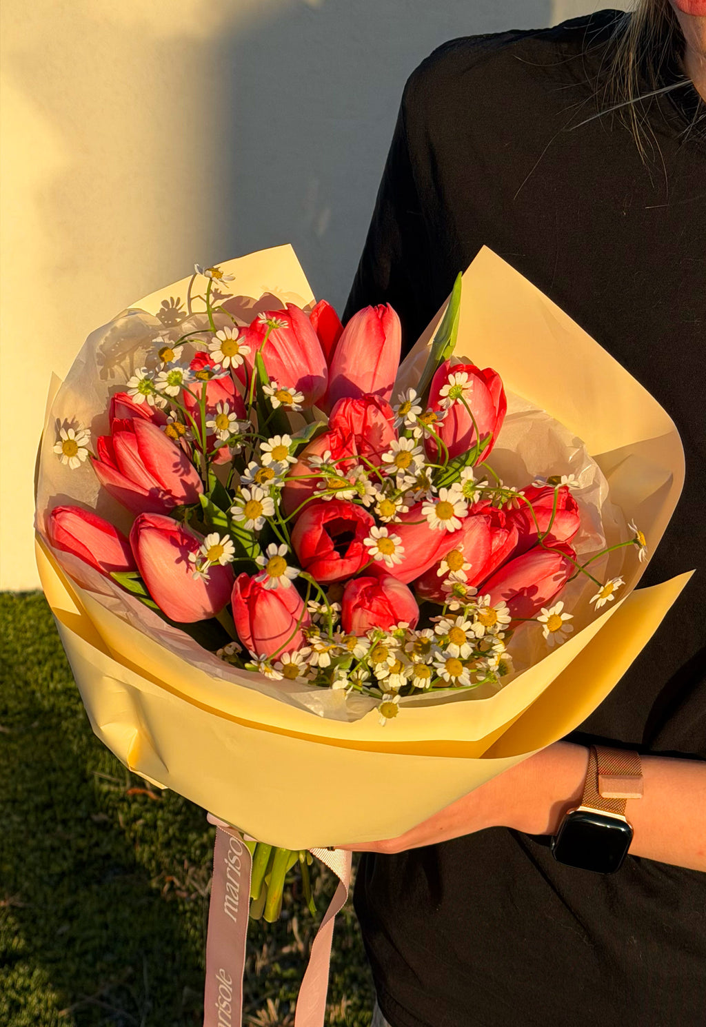 Bouquet of red tulips with greenery held by a person outdoors.