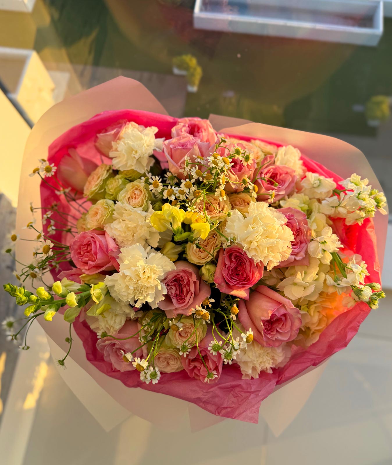 Bouquet of flowers wrapped in pink paper held by a person.