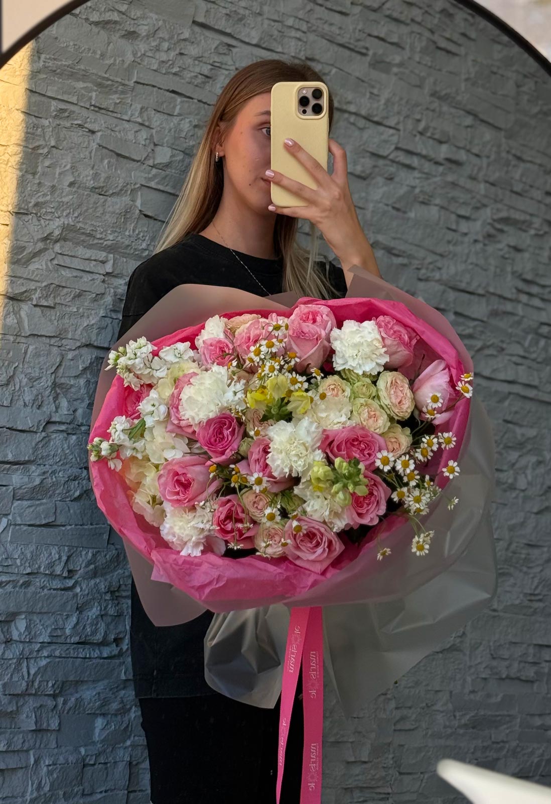 Person holding a large bouquet of flowers in front of a stone wall.