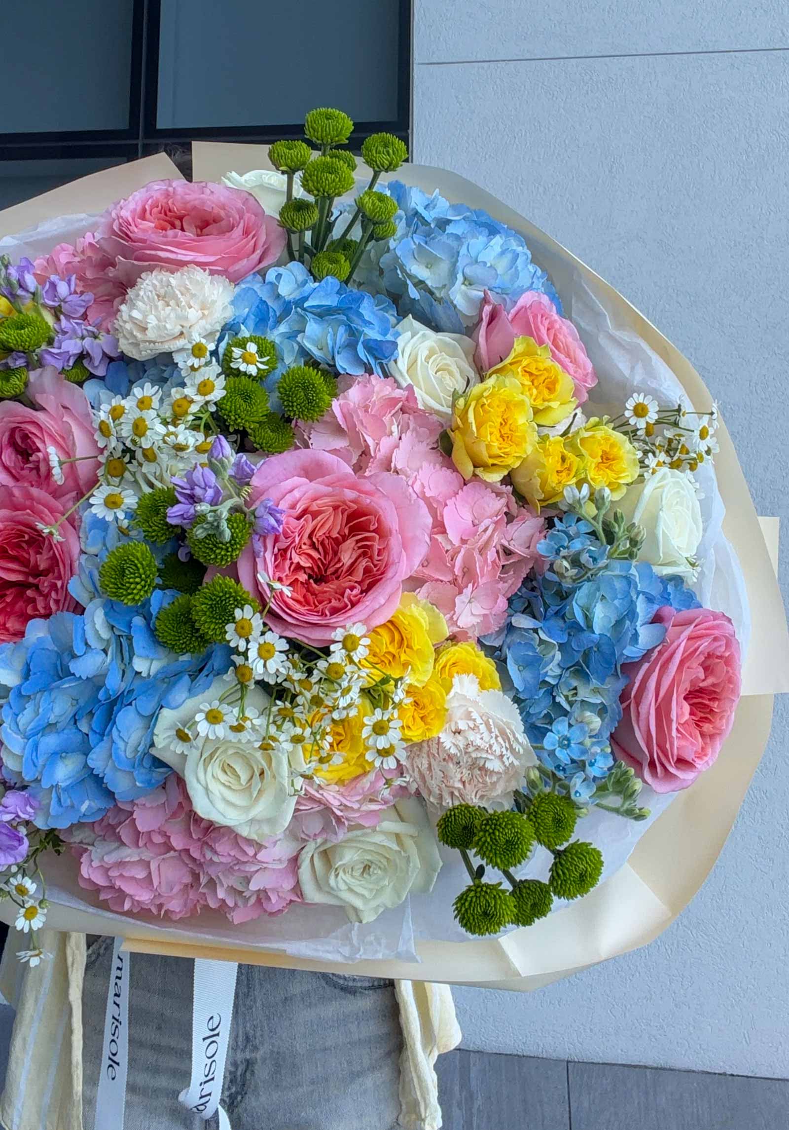 Detailed view of Unicorn Bouquet featuring pink garden roses, blue hydrangeas, yellow spray roses, white roses, chamomile, and green chrysanthemums.