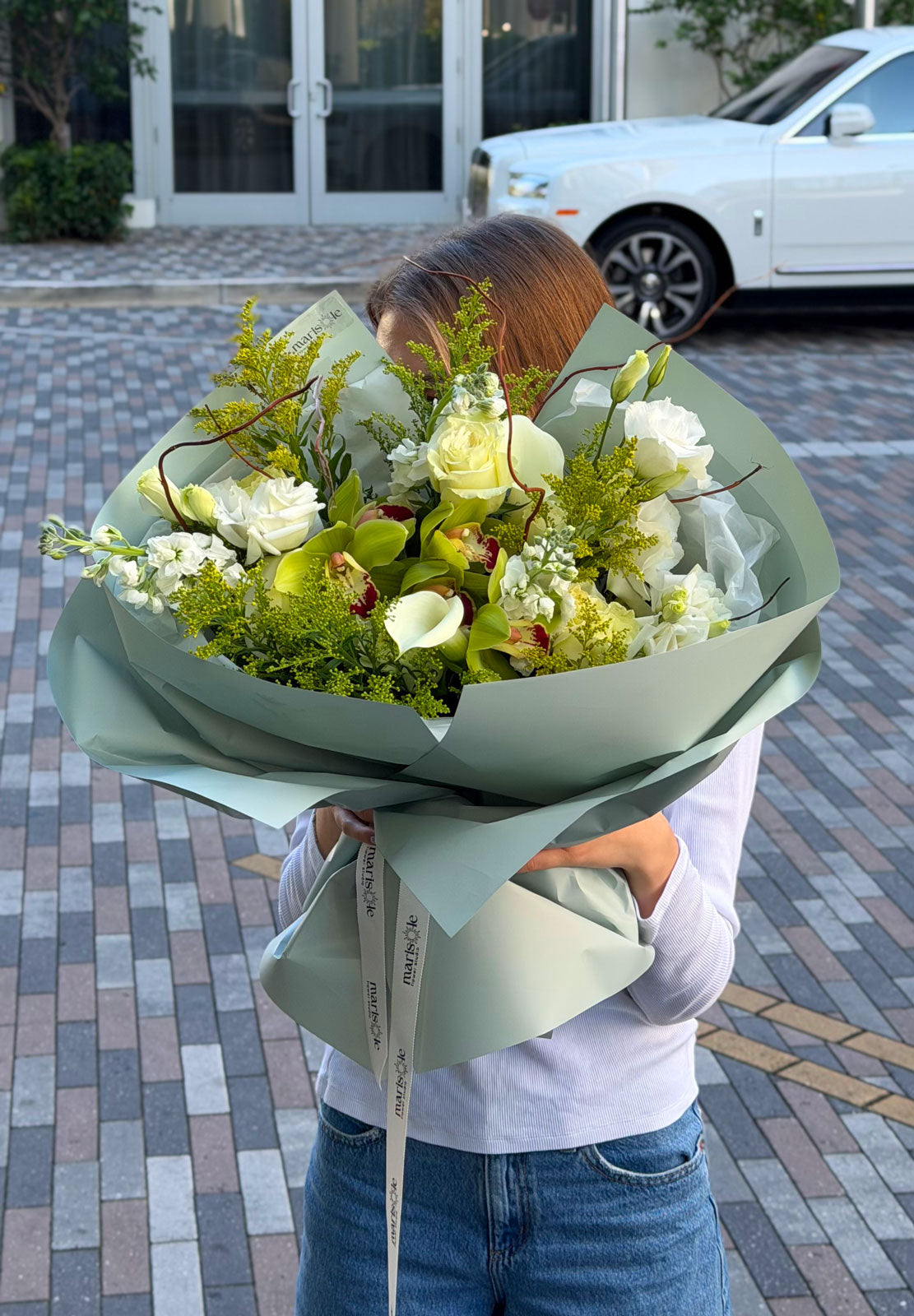 Person holding a bouquet of flowers outdoors on a paved area.