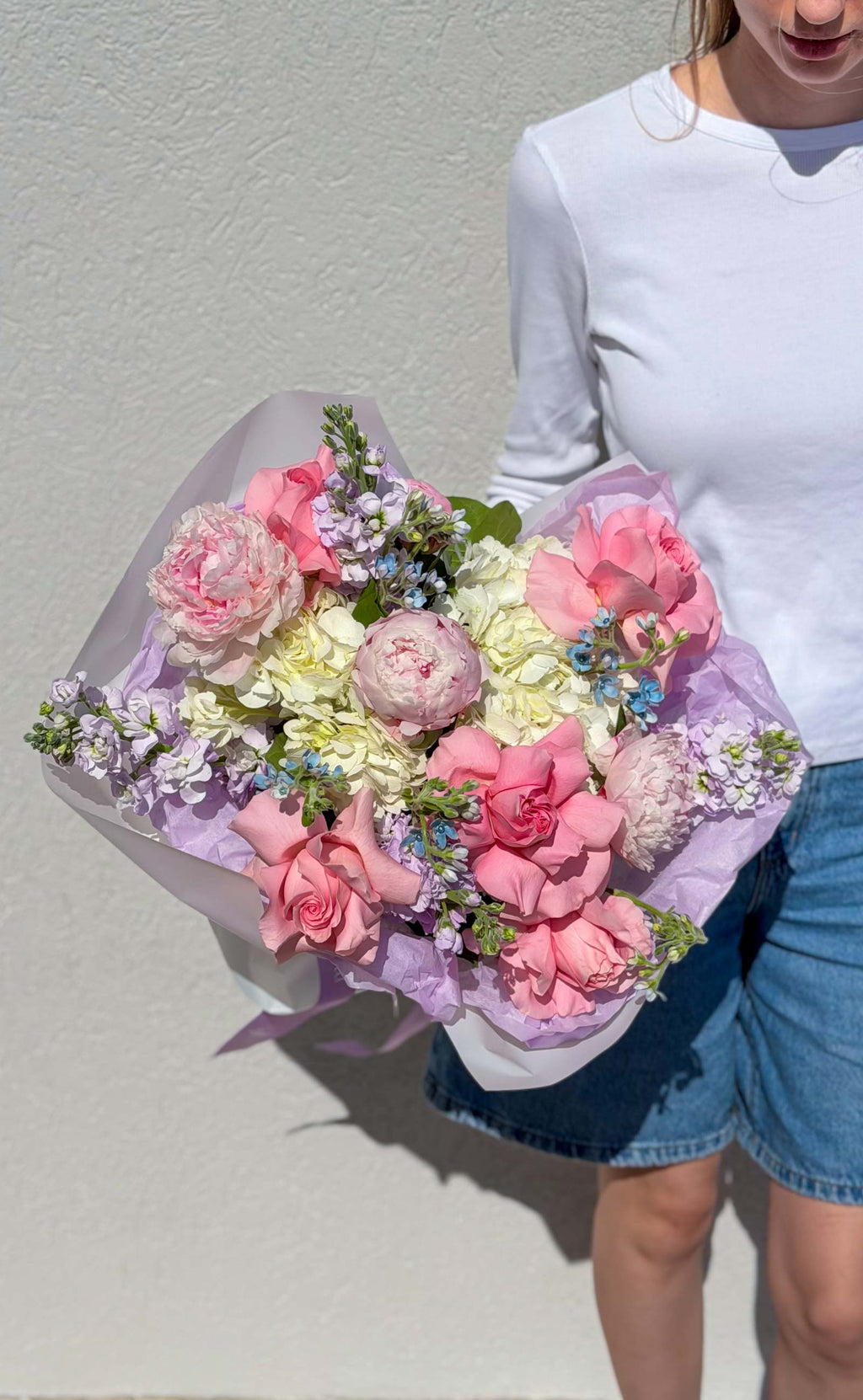 Person holding a bouquet of pink and white flowers against a plain background