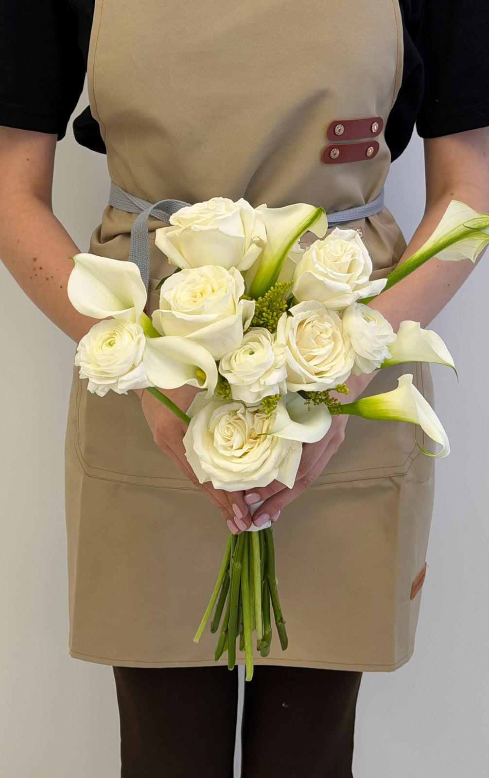 Person holding a bouquet of white flowers wearing a beige apron.