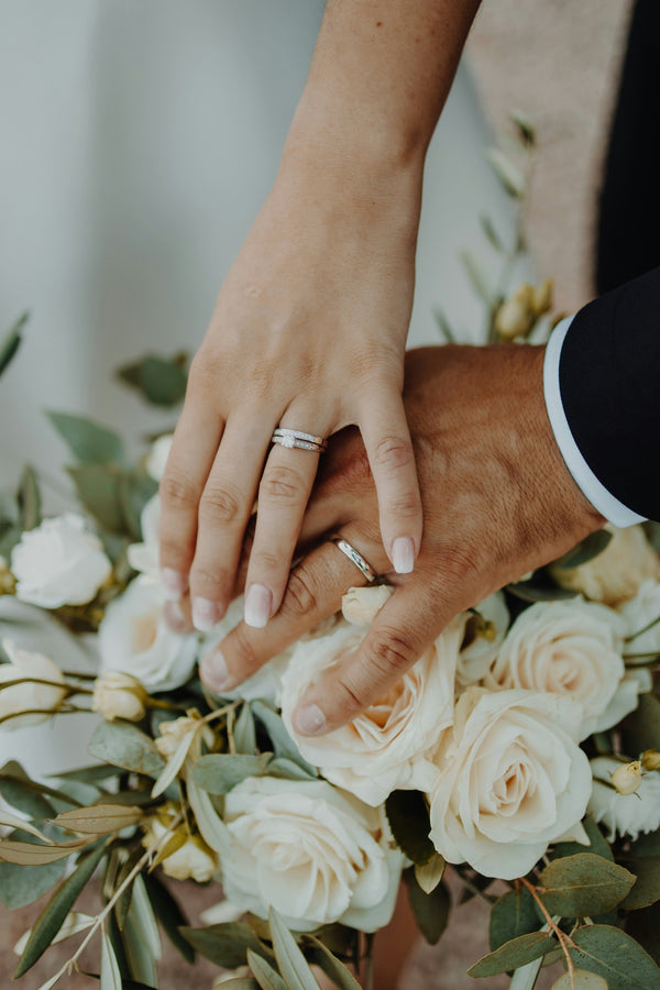 Two hands with wedding rings held over a bouquet of white flowers.