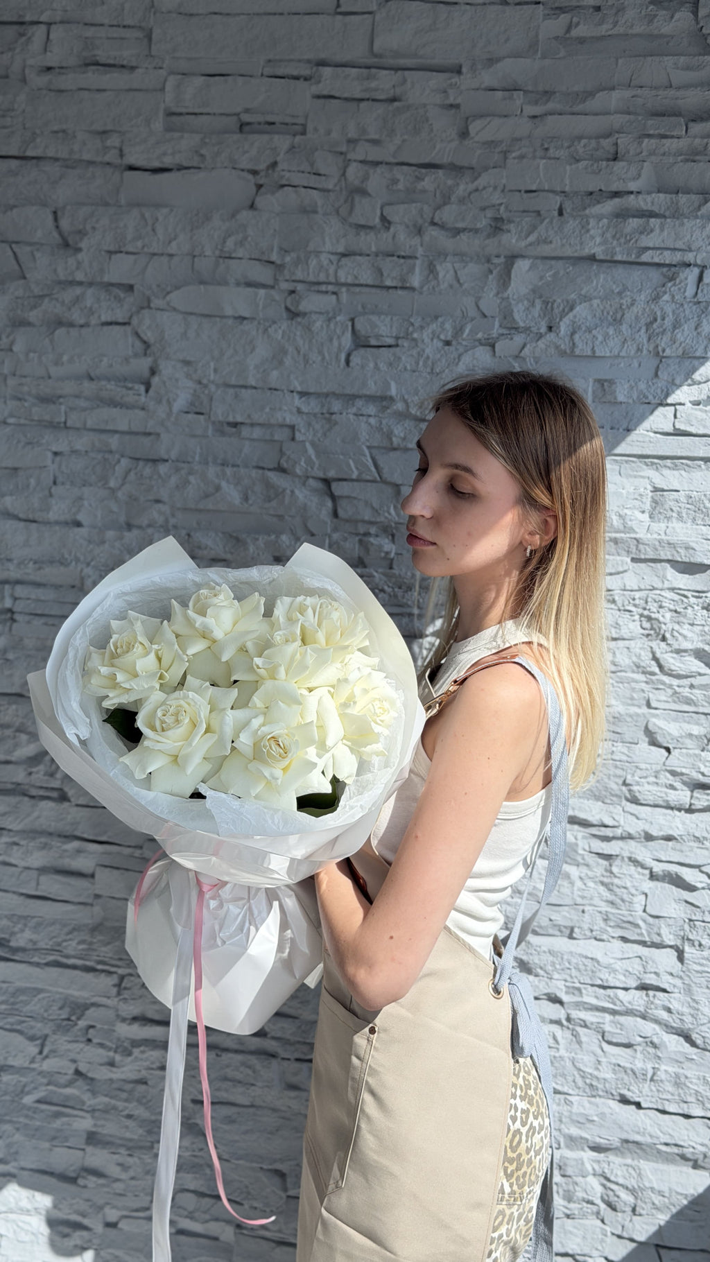 Woman holding a large bouquet of white flowers against a stone wall.