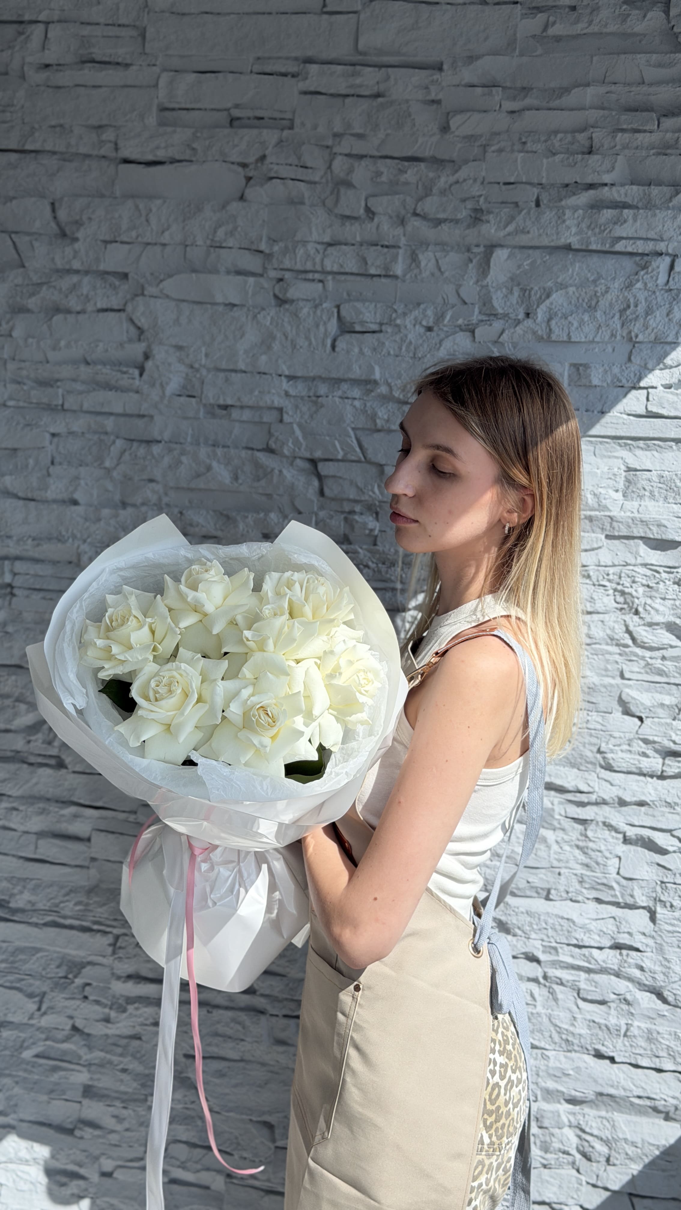 Woman holding a large bouquet of white flowers against a stone wall.