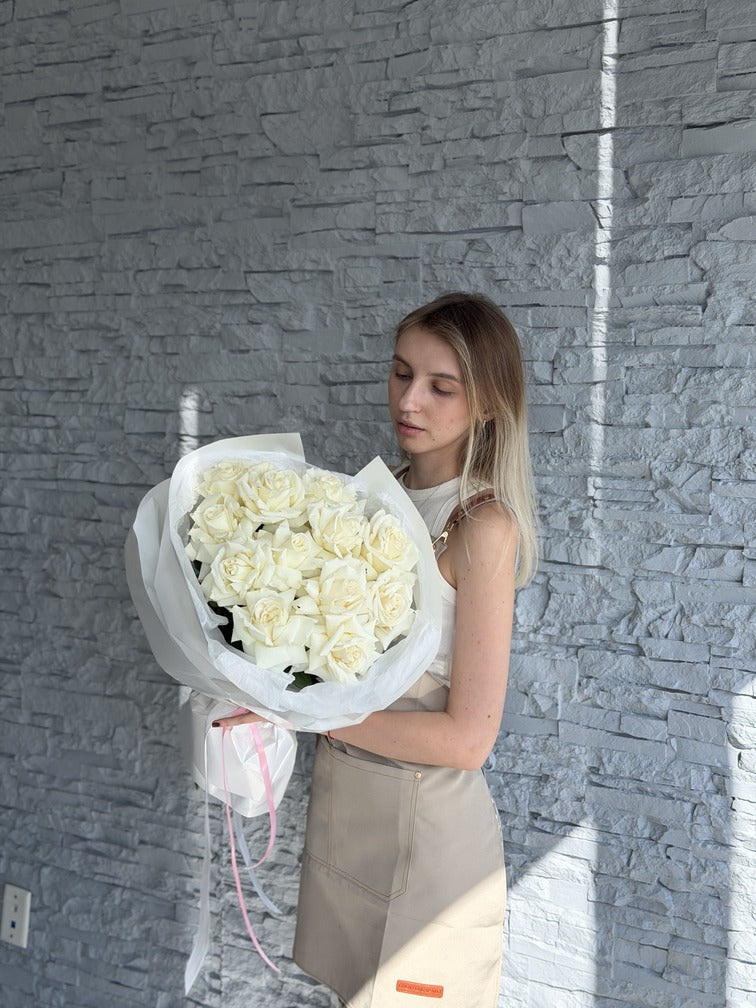 Woman holding a large bouquet of white flowers against a gray stone wall.